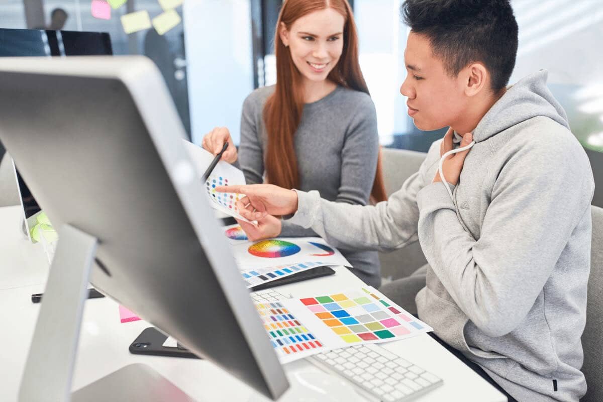 Graphic designers looking at color swatches behind computer