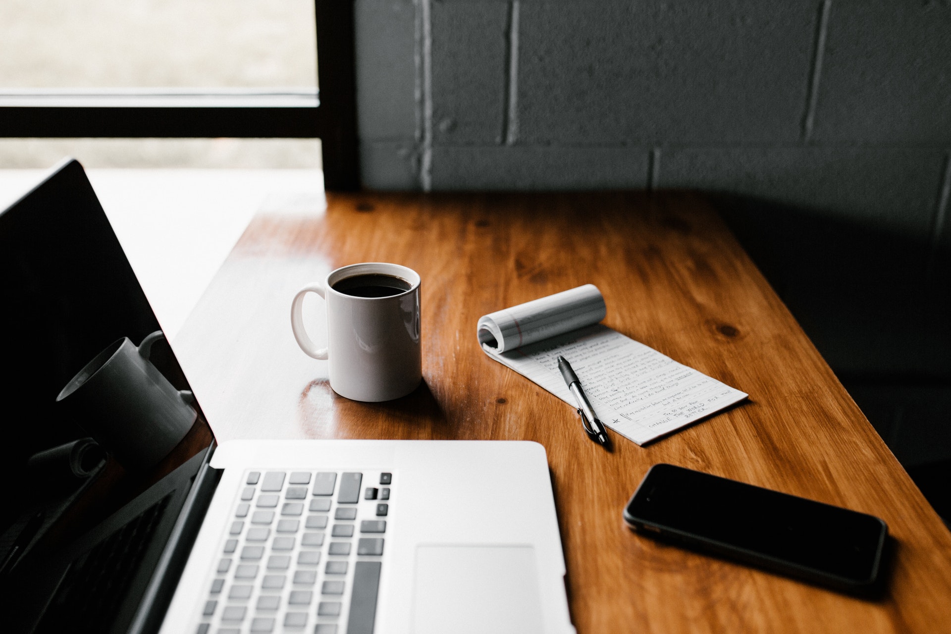 desk with laptop computer, coffee cup, cell phone and notepad with pen