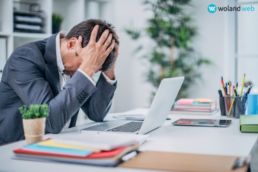 Business man sitting at desk with his head in his hands in frustration in front of an open laptop.